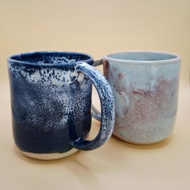 Océan et brume Deux tasses en céramique, l'une bleue marbrée et l'autre beige avec des nuances rouges.