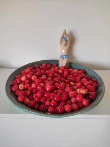 Le plongeur Plat en céramique rempli de cerises rouges, avec une figurine de nageuse à côté.
