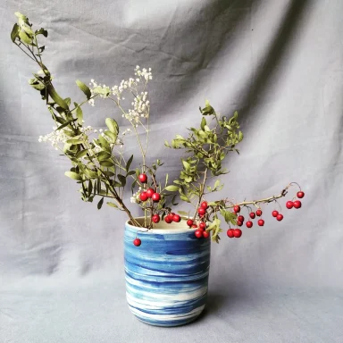 Entre vents et mers Vase en céramique bleue avec des branches de feuillage et des baies rouges.